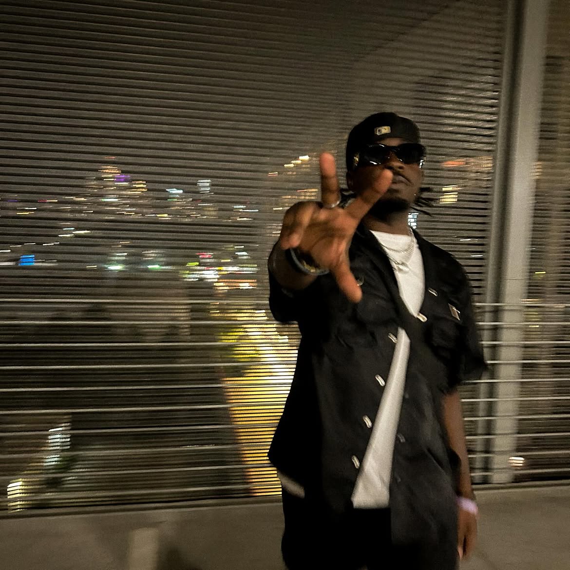 Yari in black streetwear and sunglasses by city lights